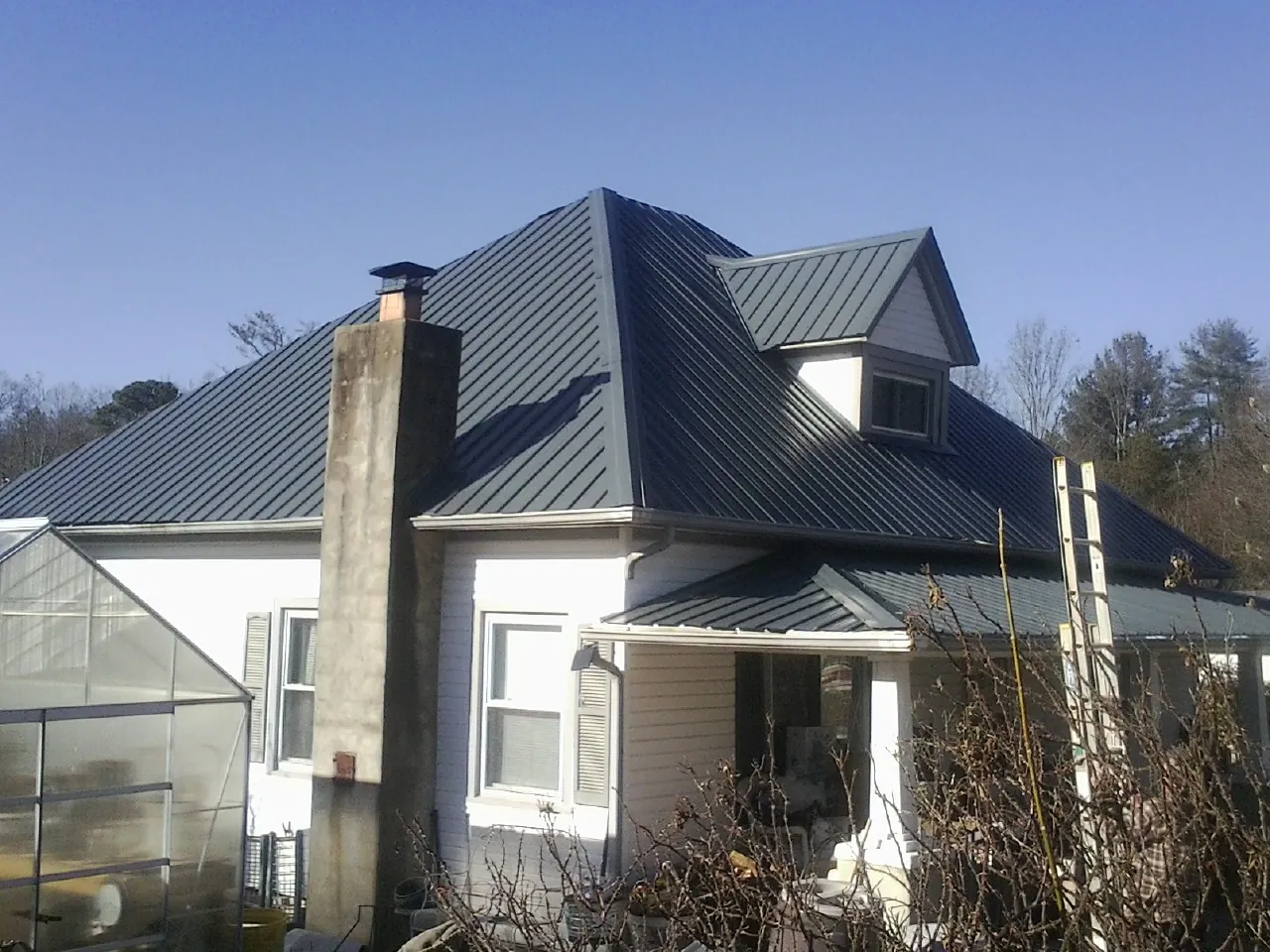 Dark blue standing seam metal roof on a white farmhouse with dormer — Slate & Tile Roof Repair by Roofing Brothers in Lesterville