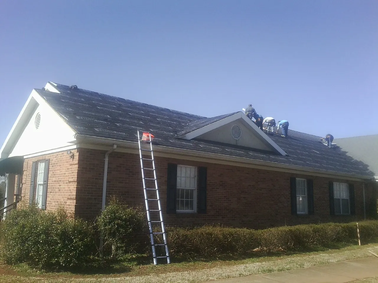 Crew tearing shingles off a brick ranch roof with a ladder set — Emergency Roof Repair work by our crew in Lesterville