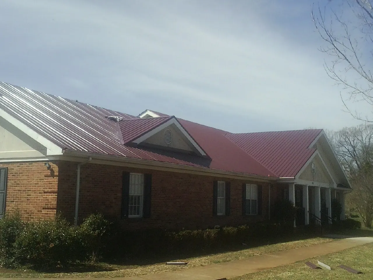 Red metal roof with gabled entries on a long brick building, from a Hail Damage Roof Repair job in Lesterville