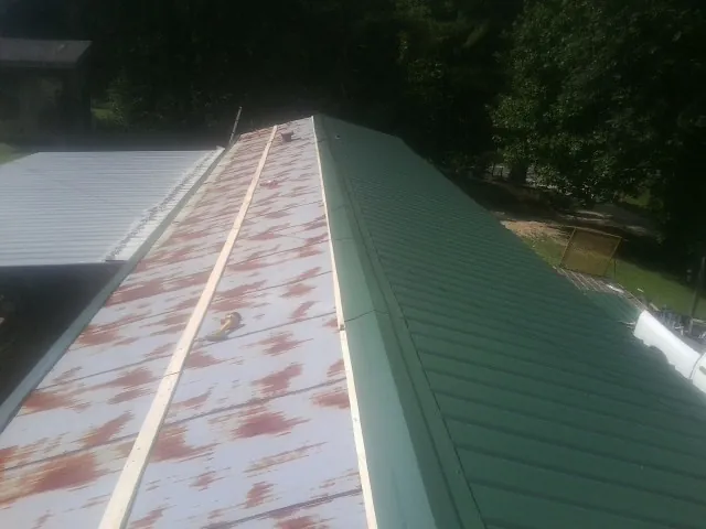 Old rusted panels beside newly installed green metal roofing — Wind Damage Roof Repair by Roofing Brothers in Lesterville