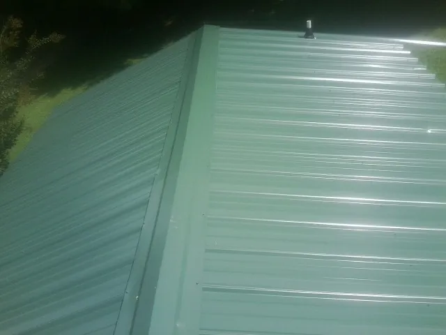 New green metal panels meeting at the ridge of a roof — Flat Roof Repair work by our crew in Lesterville