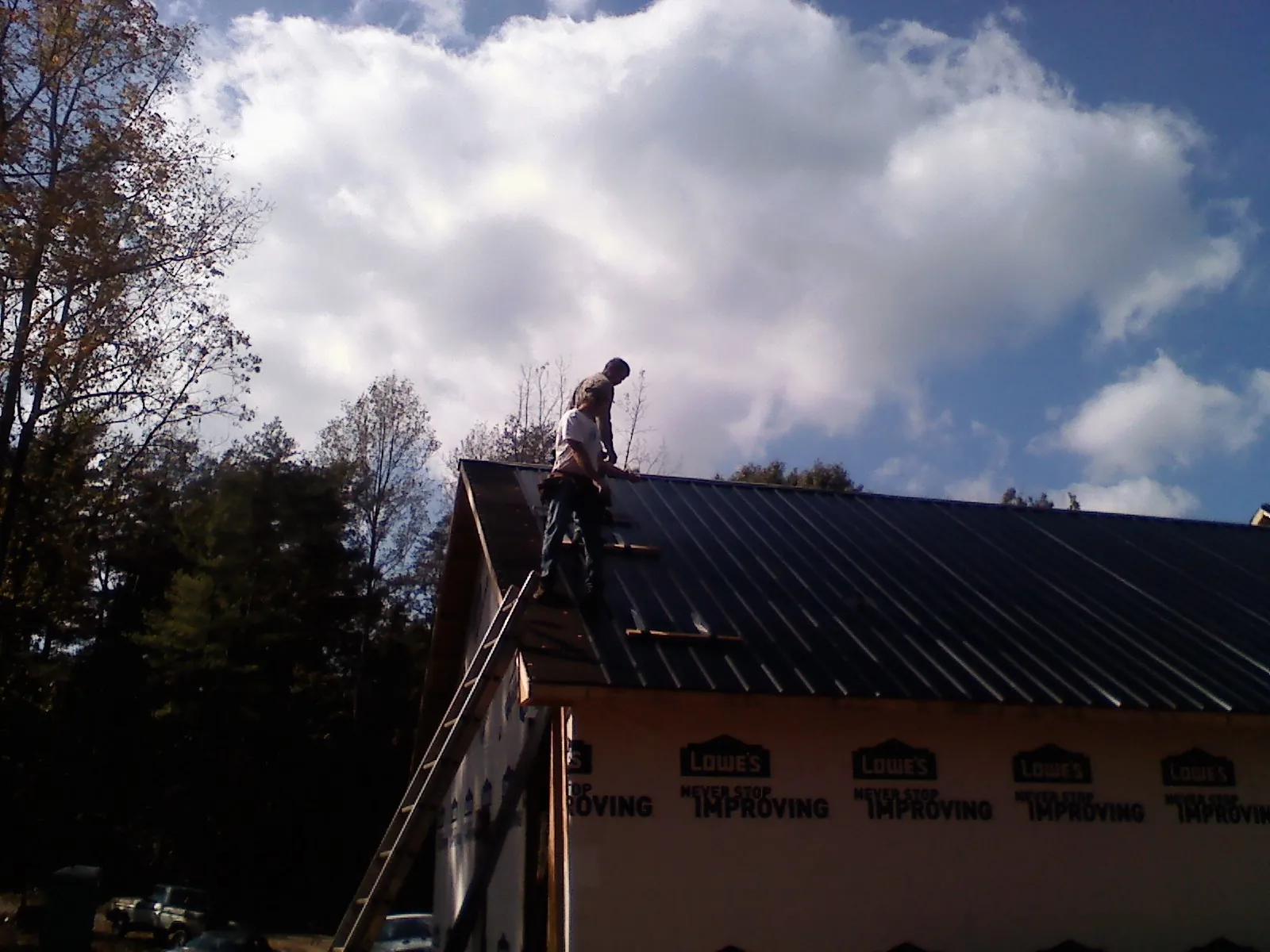 Roofer fastening dark metal panels high against a cloudy sky, from a Roof Inspection job in Lesterville