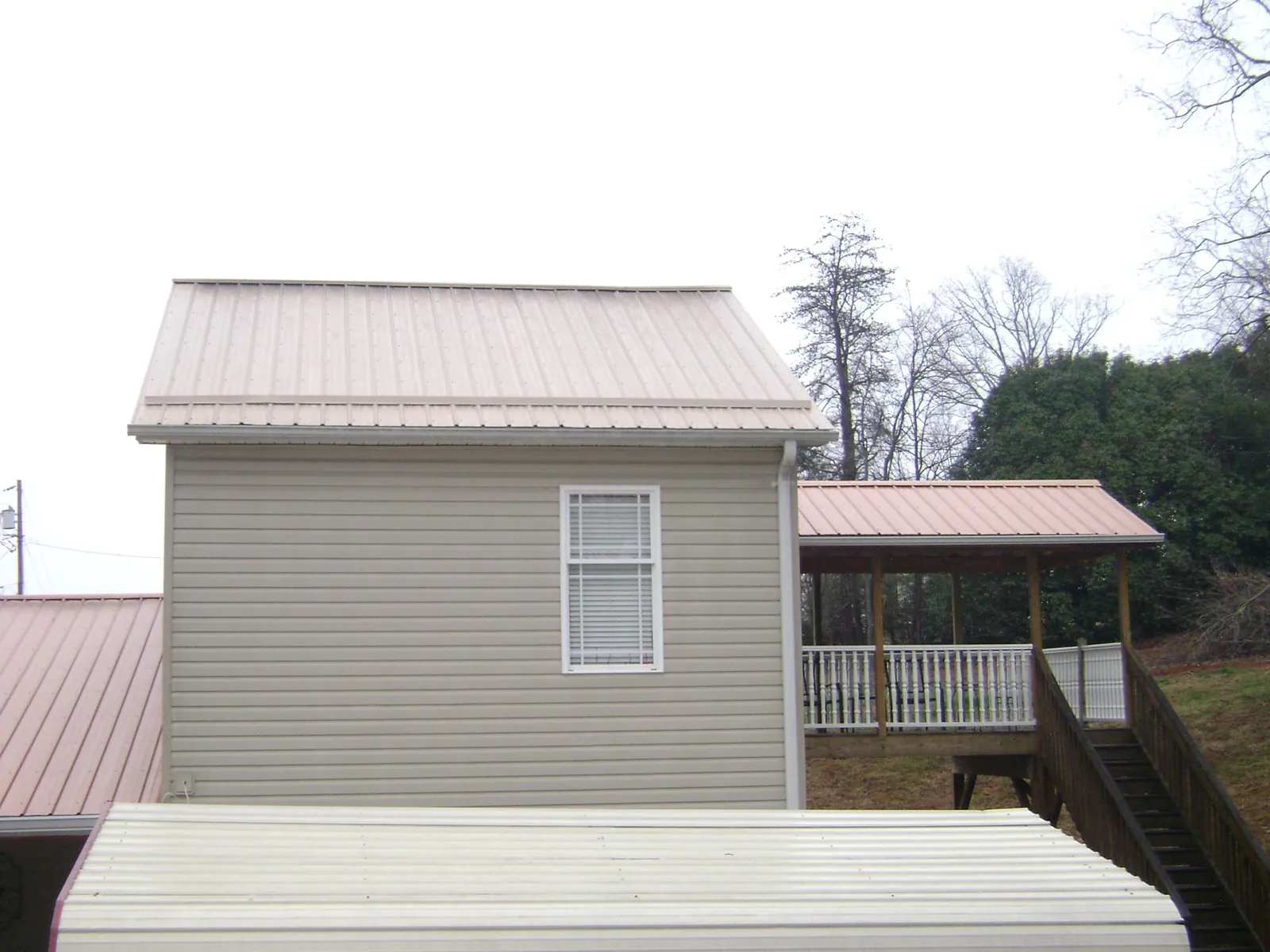 Tan metal roofs on a two story addition and attached porch, from a Roof Replacement job in Lesterville